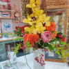Tall arrangement with yellow orchids, orange blooms, pink protea and red berries in a white rectangular vase.