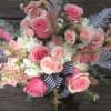 Pink roses and pale blooms arranged with a striped ribbon on wood