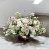 Low floral arrangement of white and blush blooms in a red container