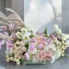 Large pastel floral arrangement with roses, orchids, and white blooms in a low container