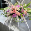 Low arrangement of pink and peach roses with pampas grass in a white container