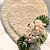 Heart-shaped white floral arrangement with pale pink roses and tropical leaves