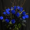 Arrangement of vivid blue roses in a tall vase with curly branches