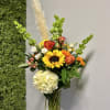 Mixed bouquet in a clear glass vase with sunflowers, roses, hydrangea, and orange blooms