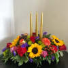 Floral centerpiece with three gold taper candles and bright mixed blooms
