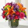 Bouquet of orange lilies, pink roses, and purple flowers in a glass vase