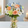 Bouquet of peach roses, white daisies, and blue flowers in a glass vase