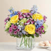 Yellow roses and pastel mixed flowers in a clear square vase