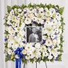 White floral funeral wreath with a photo in the center and blue ribbon