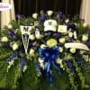 Large funeral spray with white roses, purple flowers, and a blue ribbon