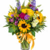 Mixed bouquet of sunflowers, roses, and purple flowers in a glass vase with a yellow ribbon