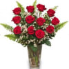Red roses arranged in a clear glass vase with fern accents