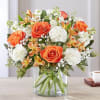 Orange roses and white flowers in a clear glass vase
