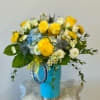 Yellow roses and mixed white flowers in a blue vase with a ribbon