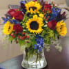 Bouquet of sunflowers, red roses, and blue flowers in a glass vase