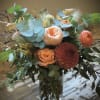 Peach and coral bouquet in a glass vase with blue-green foliage
