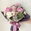 Hand-tied bouquet of pink and white flowers wrapped in dark paper with a satin ribbon.