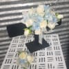 White rose bouquet with pale blue accents and ribbon on a black stand