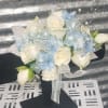 White roses and pale blue flowers arranged with ribbons on a black stand