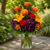 Bouquet of orange roses, yellow lilies, and purple hydrangeas in a glass vase