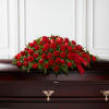 Red rose casket spray with a red ribbon on a dark casket
