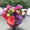 Colorful mixed bouquet in a burgundy vase with orchids, roses, and hydrangeas