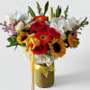 Tall mixed arrangement with sunflowers, red roses, orchids and gerberas in a yellow-wrapped vase with ribbon and butterfly