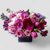 Low arrangement of purple orchids, pink roses, tulips, and mums in a dark square vase