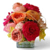 Mixed bouquet of pink, peach, red, and yellow flowers in a square glass vase