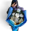 Handheld bouquet of white and purple flowers wrapped in blue paper