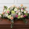 Casket spray with pastel roses, hydrangeas, and trailing greenery