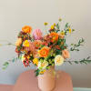 Mixed bouquet of orange, pink, and cream flowers in a blush vase