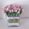 Pink tulips arranged in a clear square vase with a lavender ribbon