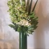 Tall green floral arrangement with orchids and calla lilies in a glass vase