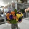 Mixed roses in orange, yellow, purple, and pink in a glass vase
