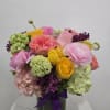 Colorful bouquet of roses and ranunculus in a glass vase with a purple ribbon