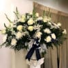 Large white floral arrangement in a pedestal vase with a ribbon bow