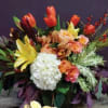 Low arrangement of orange tulips, yellow lilies, white hydrangea, and roses in a container