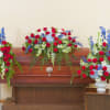Red, white, and blue funeral floral set with casket spray and side arrangements on a wooden casket