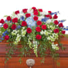 Red, white, and blue casket spray with roses, carnations, and mixed flowers on a wooden casket
