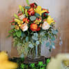 Tall bouquet of orange roses and yellow lilies with cream roses in a clear glass vase