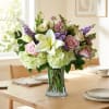 Bouquet of white lilies, roses, and purple flowers in a glass vase