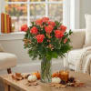 Orange roses in a glass vase on a table with pumpkins and a candle