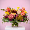 Colorful arrangement of yellow calla lilies, roses, tulips, and protea in a clear glass cube vase