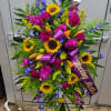 Standing spray of sunflowers, lilies, and purple flowers with a mourning ribbon