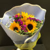 Bouquet of sunflowers and small purple flowers wrapped in pale paper