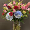 Mixed bouquet of roses, lilies, hydrangeas, and pink blooms in a glass vase