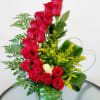 Red roses arranged in a clear glass vase with yellow filler flowers