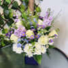 Mixed bouquet of white roses, purple flowers, and white daisies in a blue vase