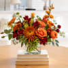 Orange and burgundy flowers in a glass vase on stacked books
